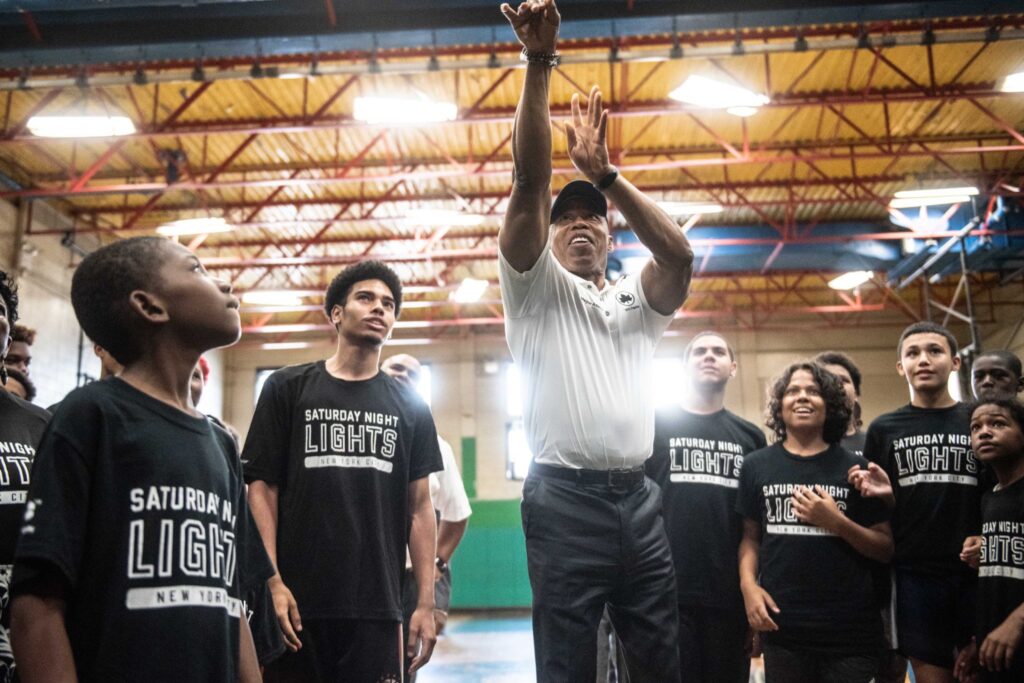 Mayor Adams shooting basketball while youth look on.